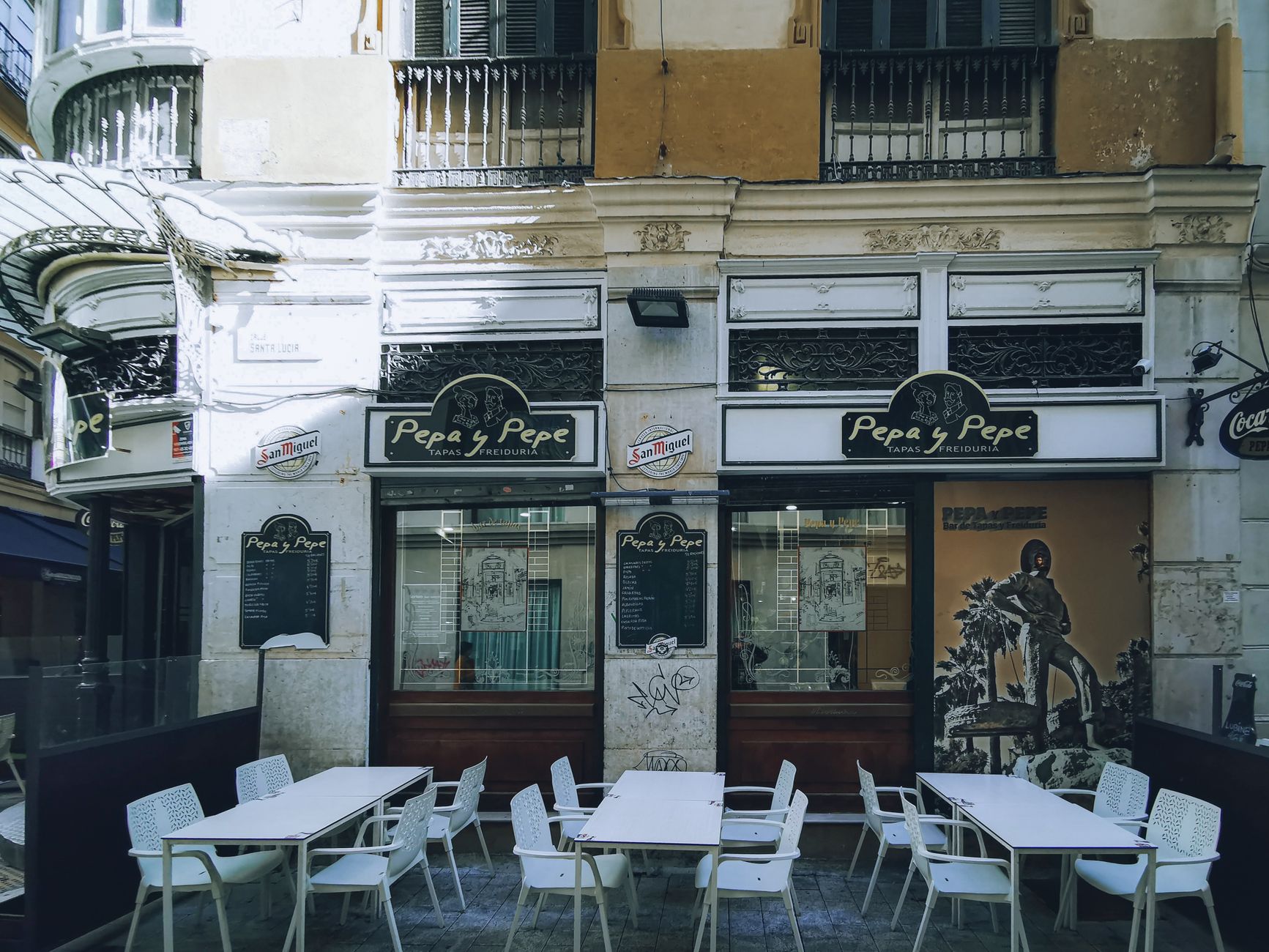 Terraza exterior de un bar con mesas y sillas en una plaza de San Vicente del Raspeig